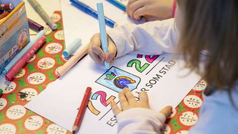 A child colors the Espoo 50 years as a city -logo.