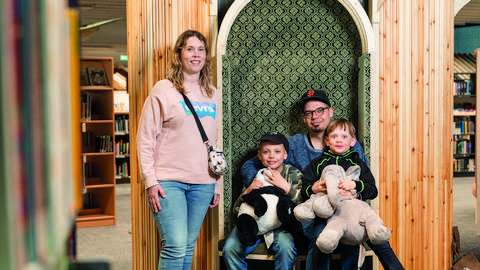 A family of four in the library - dad sitting with their boys in his arms and mom standing next to them.