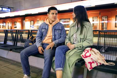 Två unga vuxna som sitter på en bänk på en metrostation.