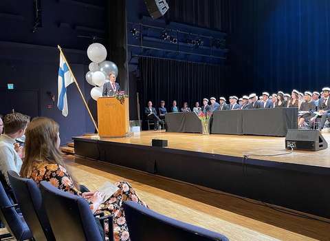 Abiturientit kuuntelevat lavalla vanhemman puhetta. 