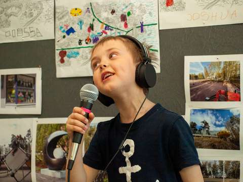 Viisivuotias lapsi laulaa mikrofoniin kuulokkeet päässä musiikkivideon nauhoituksissa.