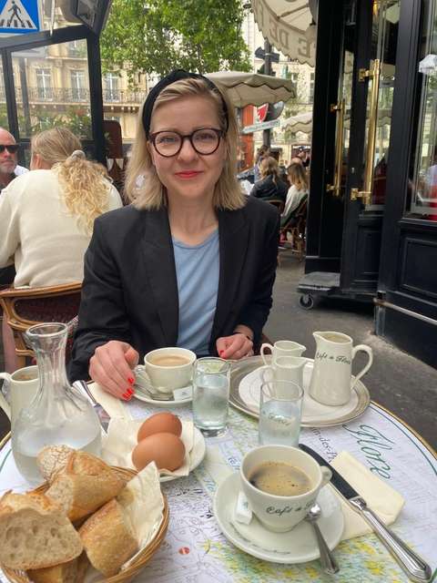 Emma istuu kahvilassa kaupungin vilinä takana. 