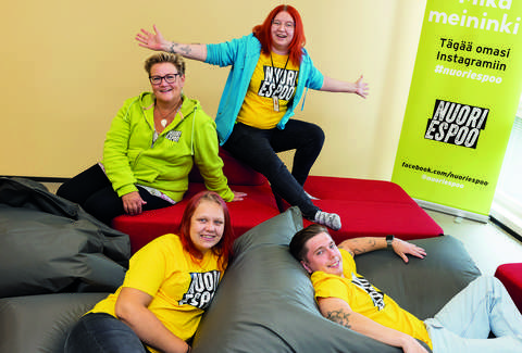 Four adults in colourful Nuori Espoo t-shirts and hoodies sitting on beanbag chairs.