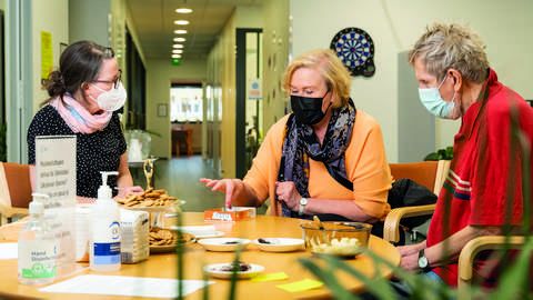 Tre personer med masker över ansikten vid ett runt bord.