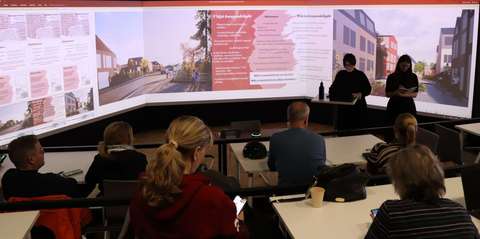 Föreläsningssal, människor, på projektorduken illustrationer av glesbebyggda och tätbebyggda stadsmiljöer.