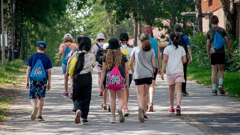 Ryhmä kesäleiriläisiä kävelemässä takaapäin kuvattuna. Osalla Nuori Espoo -reput selässä. 