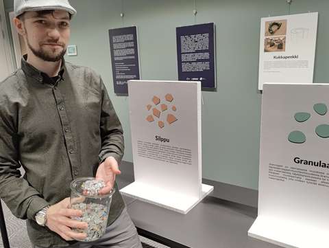 Eetu Mäntynen står leende framför utställningstavlorna med en burk strimlad plast i handen.