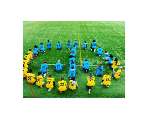 Opiskelijat muodostavat rauhanmerkin. Osalla on keltainen paita ja osalla turkoosi paita.