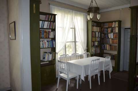 Villa Rulluddin kirjaston hyllyjä ja valkoinen ruokapöytä tuolineen. 