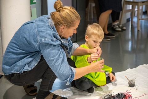 Päiväkodin työntekijä auttaa lasta maalaamisessa.