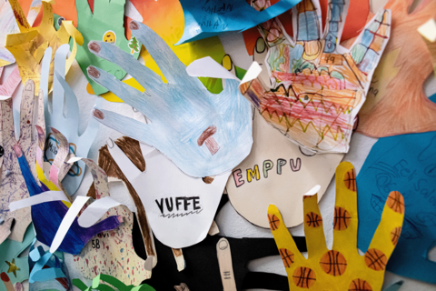 Lasten värikkäitä paperista askarreltuja kämmeniä seinällä.