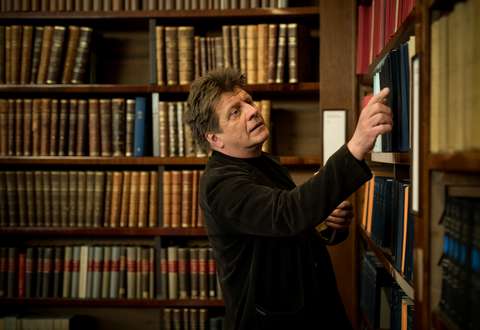 Timo Torikka valitsee kirjaa kirjahyllystä.