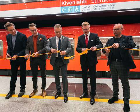 Mika Nykänen, Matias Pajula, Jukka Mäkelä, Juha Hakavuori ja Ville Saksi seisovat rinnakkain ja pitelevät käsissään oranssia nauhaa ja saksia, joilla leikkaavat nauhan poikki. 