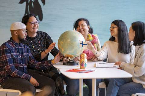 Viisi kulttuuriohjaajaa istumasssa pöydän ääressä karttapalloa tutkiskellen. 