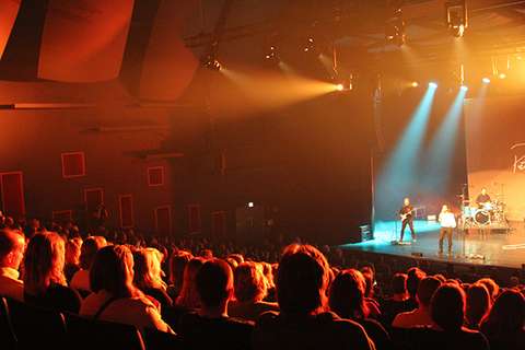 Täysi katsomo oranssissa valaistuksessa musiikkikeikalla Sellosalissa.