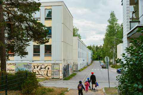 Ett tomt hyreshus med graffiti målat på stengrunden. Bredvid byggnaden ligger en gata längs vilken två barn och en vuxen passerar.