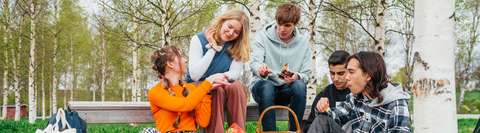 Nuoria keväällä ulkona puistossa istumassa. Nuoret opiskelevat ja syövät eväitä.