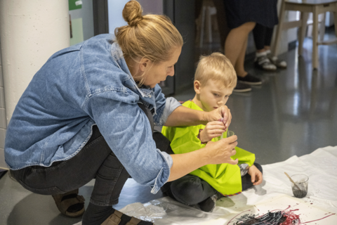 Lapsi maalaa lattialla istuen työntekijän avustamana.