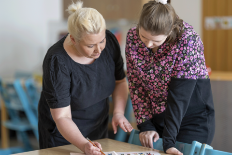 Kaksi päiväkodin työntekijää katsovat pöydällä olevaa materiaalia yhdessä.