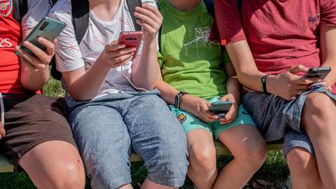 Neljä nuorta istumassa kännykät kädessä pelaamassa mobiilipeliä. 