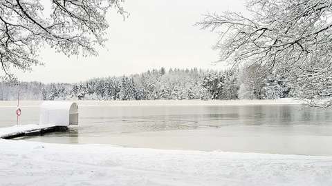 Valokuvassa näkyy jäätynyt järvi. Vasemmassa reunassa on laituri, jonka vieressä on sula kohta. Etualalla näkyy lumiasia puiden oksia.