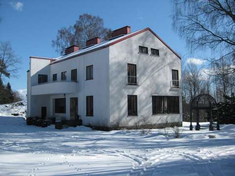 Valkoinen kaksikerroksinen kivitalo talvisessa lumisessa maisemassa. 