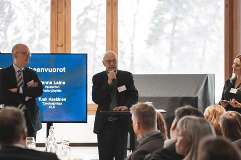 Tilannekuva puheenvuorosta. Kuvassa näkyy yleisöä ja kolme henkilöä lavalla. 