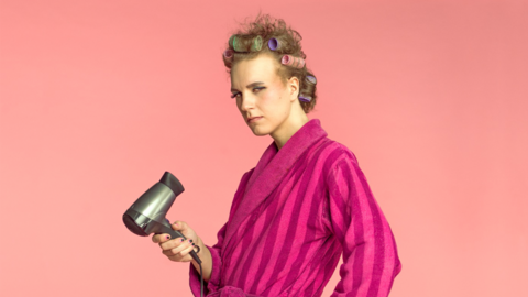 Henkilö pinkissä aamutakissa pitää kädessään hiustenkuivaajaa.