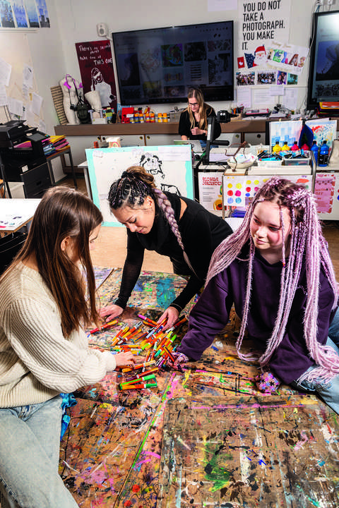 Kolme nuorta on keskittynyt piirtämään yhteistä pöydällä olevaa taideteosta.