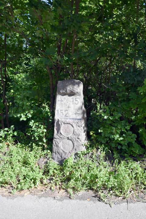 1930-luvulla rakennetun Turuntien graniittinen kilometripyläväs vihreitä puita vasten.