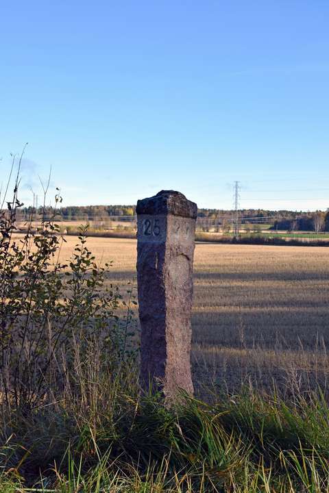 Maantien varrella, pellon reunalla graniittinen kilometripylväs.