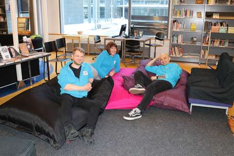 Kolme etsivää nuorisotyöntekijää istuskelee säkkituolien päällä ja katsoo hymyillen kameraan. 