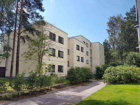 Ett lågt flervåningshus i Mattby i Esbo. Det växer gröna träd och buskar runt huset.