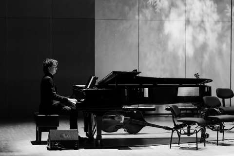 Henkilö istuu flyygelin ääressä mustavalkoisessa kuvassa.