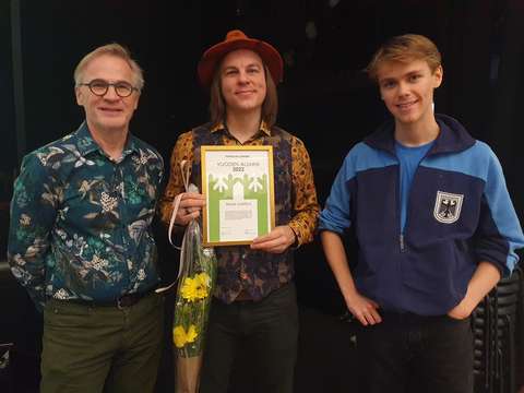 Kolme miestä seisovat vierekkäin ja hymyilevät kameralle.