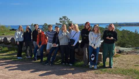 opiskelijat seisovat mäellä ja takana on meri