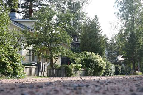 En öde gata och ett gult hus omgivet av grönska.