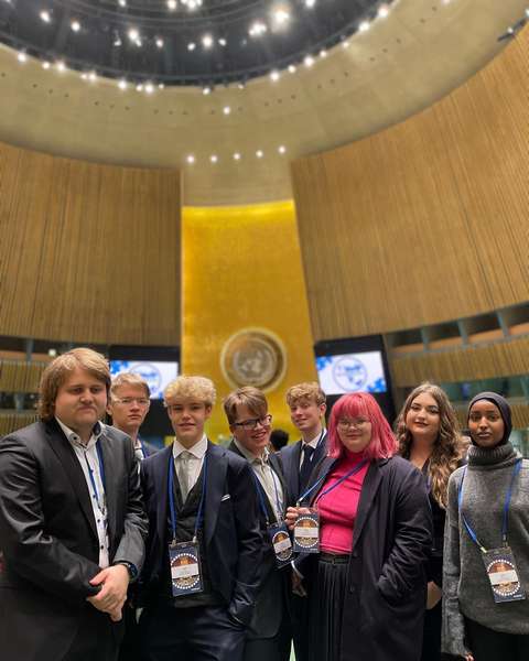 EYL:n kahdeksan delegaattia seisovat hymyille YK:n pääkonttorin salissa.