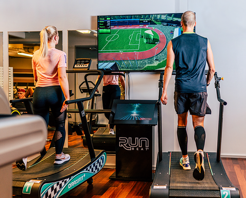 Två personer spelar motionsspel på löpband. Framför dem finns en skärm.