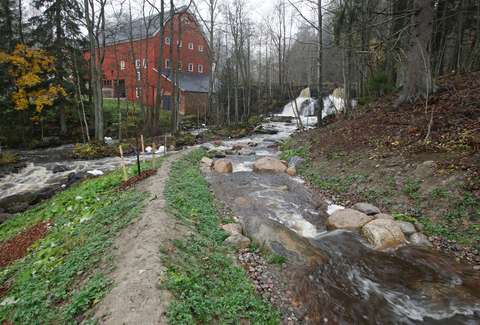 Fors med en smal stig längs stranden, i bakgrunden en röd tegelbyggnad.