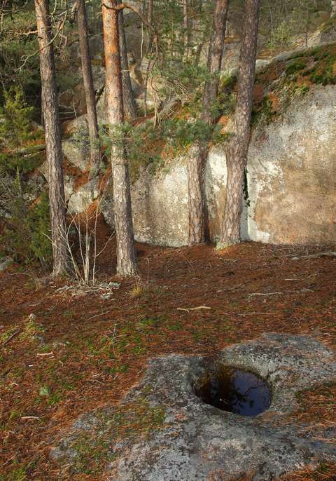Vettä täynnä oleva hiidenkirnu, jonka taustalla karua kalliota ja mäntyjä.