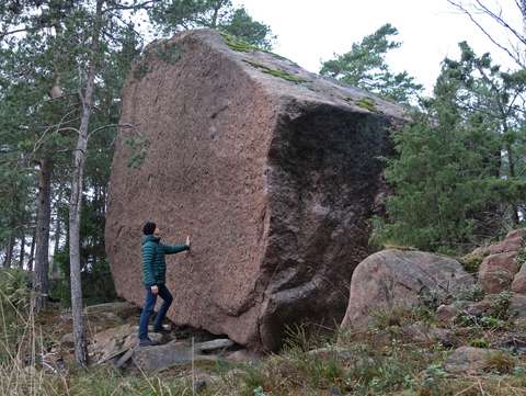 Ett stort flyttblock, alldeles slätt på fotografens sida. I förgrunden poserar en person som är mindre än hälften så hög som flyttblocket.