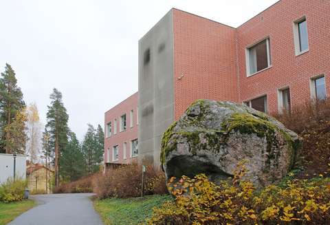 Suuri kivi, jonka taustalla kaksikerroksinen punatiilinen rakennus.
