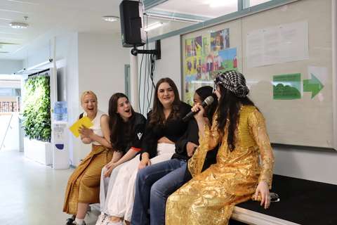 Tytöt istuvat lavan reunassa omien kulttuurien asussa, katsovat toisiinsa ja nauravat. 