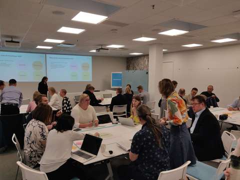 Neljä ideointiryhmää pöytien ääressä tekemässä ideamyllyvaihetta.