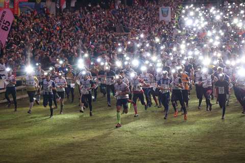 Kuvassa näkyy satoja ihmisiä juoksemassa nurmialueella otsalamput päässään. Kuvassa on hämärää.