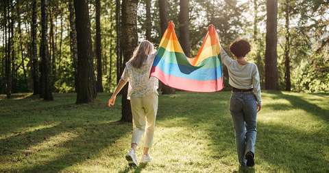 Kaksi nuorta kävelee ulkona ja kantaa välissään sateenkaarilippua.