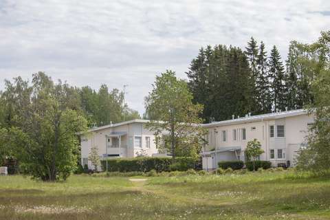 Vaalea rivitalo, jonka ympäristössä on paljon puita, nurmikenttää ja pensaita.