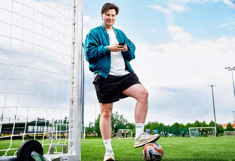 Elias Reunamo jalkopallokentällä maalin vieressä. Reunamo katsoo katsoo kameraan ja pitää käsissään älypuhelinta. Toista jalkaa Reunamo pitää jalkapallon päällä.