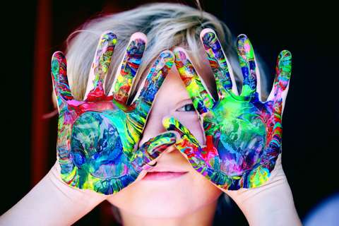 A child holding palms painted in different colors in front of his or her face.